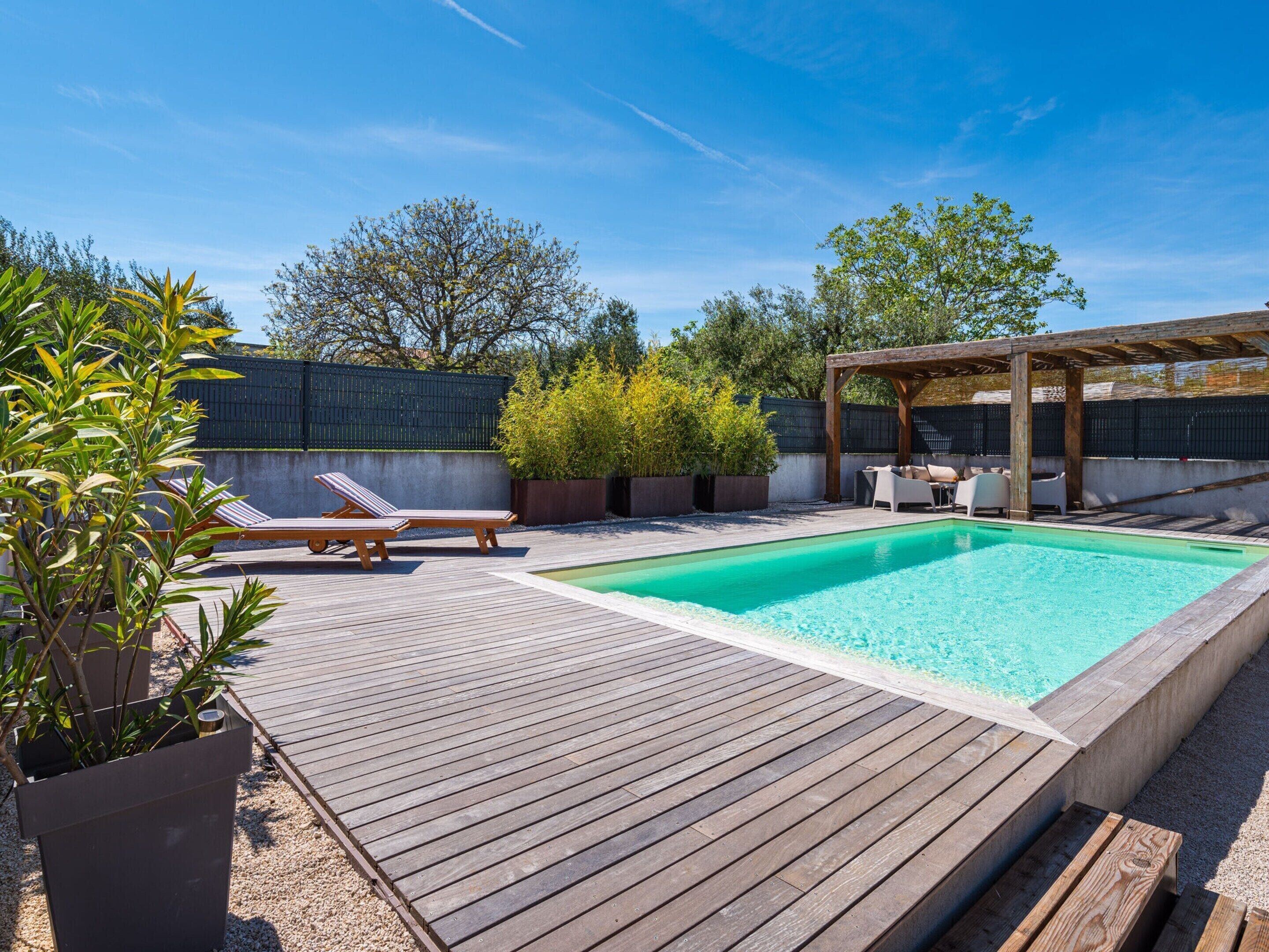 A wooden deck with a swimming pool, lounge chairs, and a pergola.