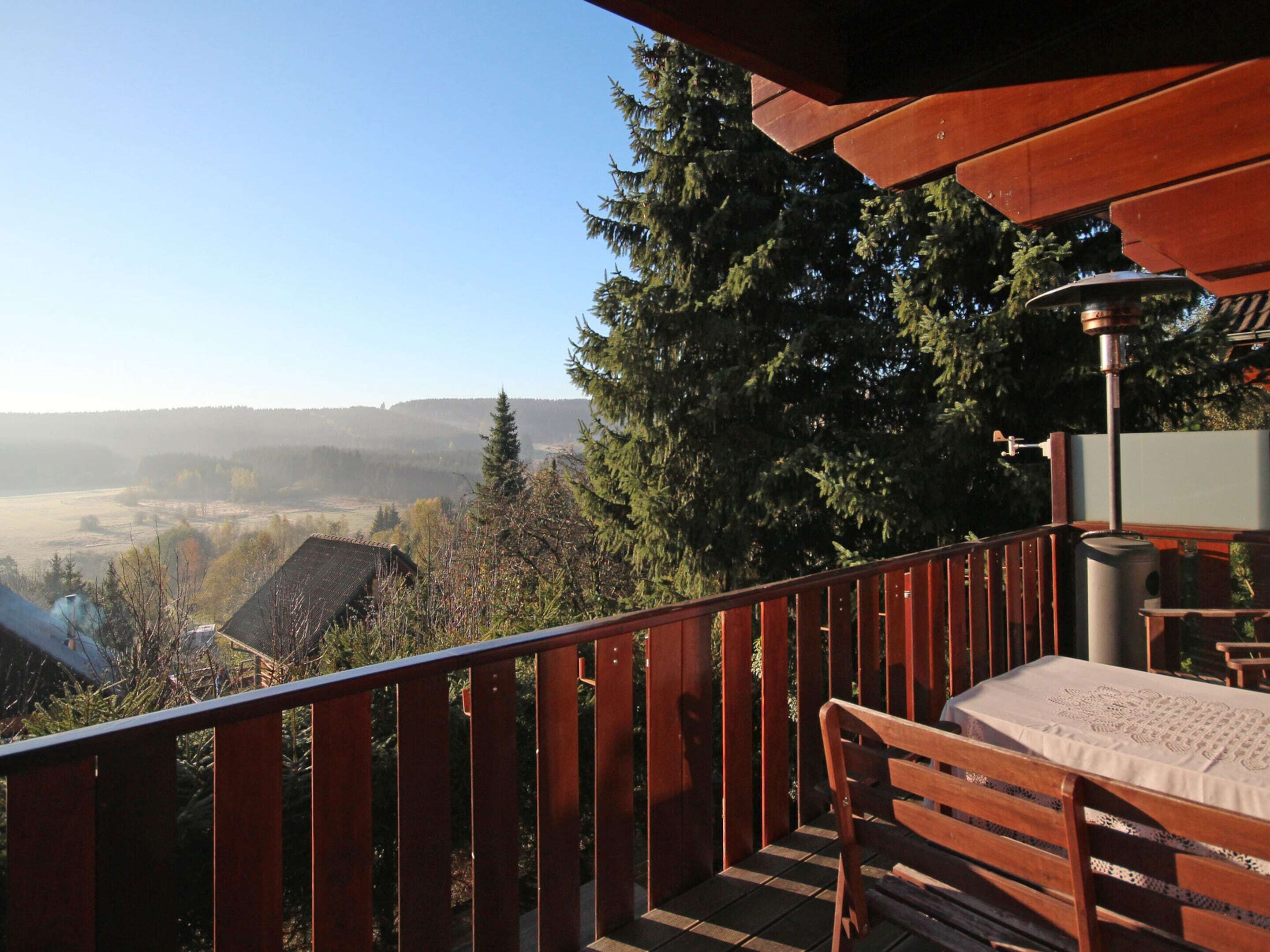 Una terraza de madera con un banco y una mesa, con vistas a un valle boscoso.