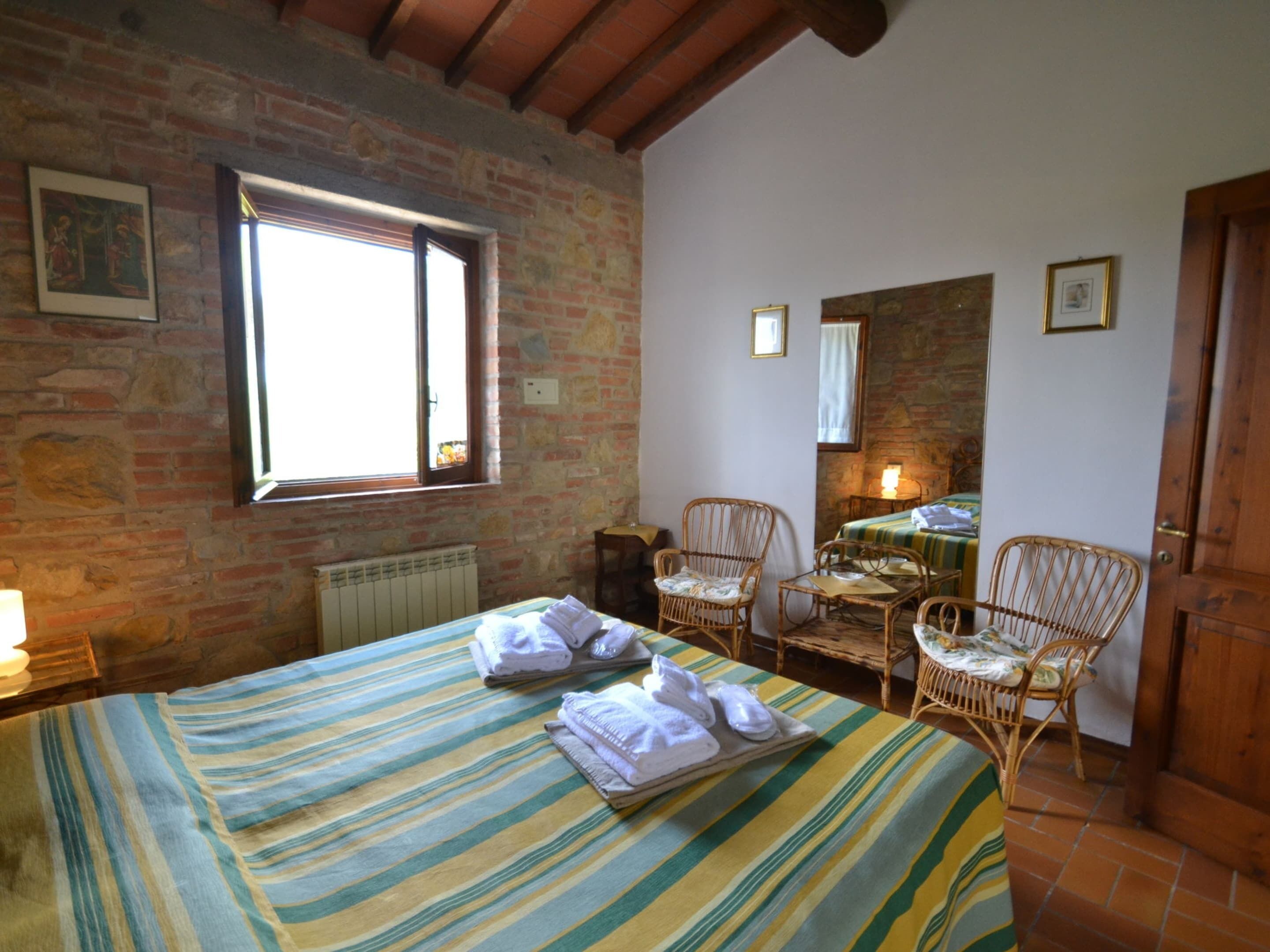 Une pièce comprenant un lit, deux fauteuils en osier, une table avec une lampe et une fenêtre.