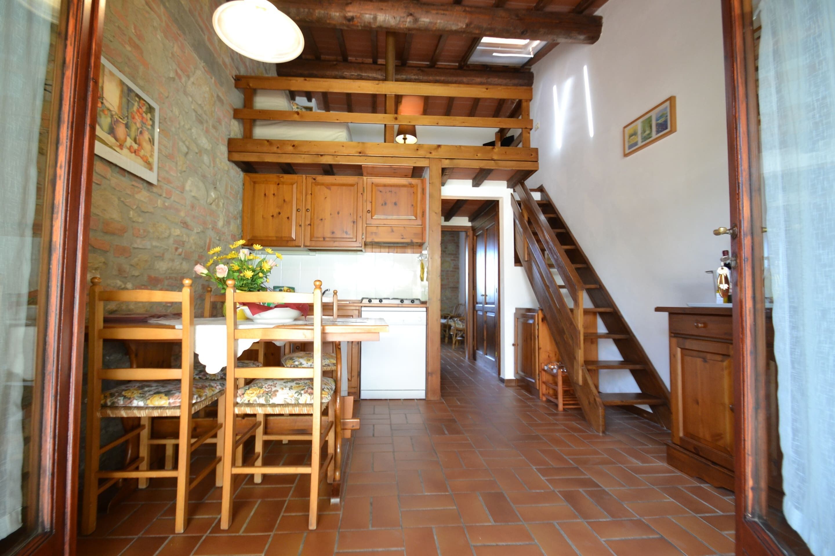 A rustic kitchen with wooden cabinets, a dining table with chairs, and a staircase leading to an upper level.