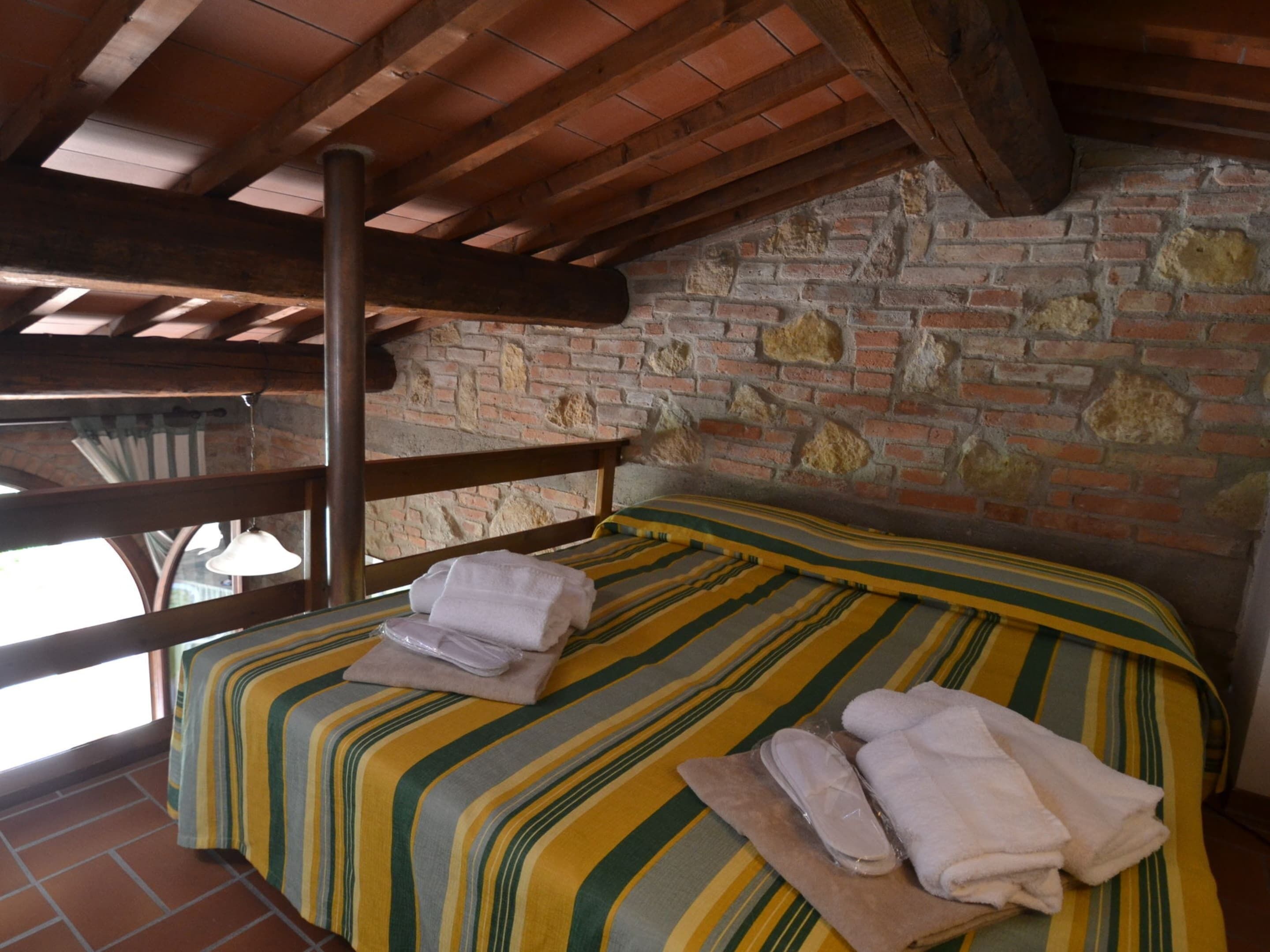 A room with a bed, wooden beams, a brick wall, and a window.