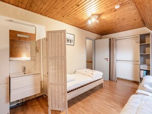 Camera da letto con soffitto in legno, un letto, un armadio, uno specchio e uno scaffale con vestiti piegati.