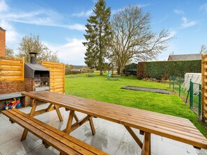 Un cortile con un tavolo di legno, un barbecue e un prato verde.