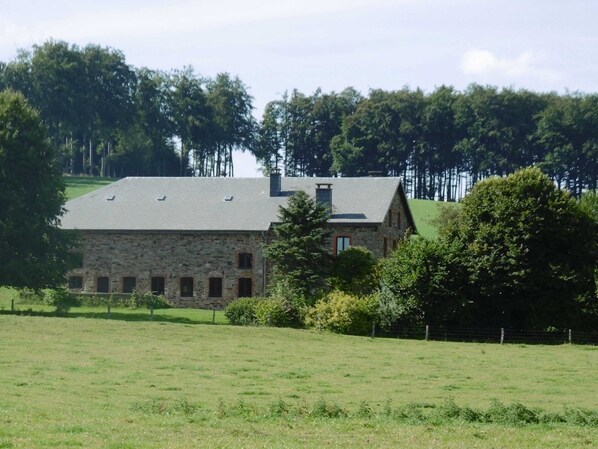 Een gebouw van steen met een schuin dak, omringd door een grasveld en bomen.