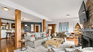 A spacious living room with a large sofa, a coffee table, and a fireplace. There is a kitchen area with wooden cabinets and a dining table. - Tremblant Prestige - Altitude 170-2 (Mont-Tremblant)