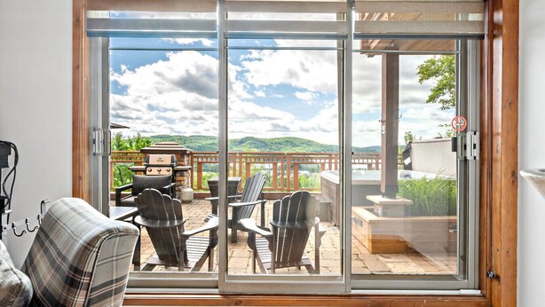 A room with a sliding glass door leading to an outdoor patio area with a grill, chairs, and a view of a mountainous landscape. - Tremblant Prestige - Altitude 170-2 (Mont-Tremblant)