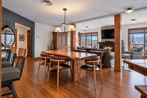 A spacious living area with a wooden dining table, comfortable seating, a fireplace, and large windows offering a view of the outdoors. - Tremblant Prestige - Altitude 170-2 (Mont-Tremblant)