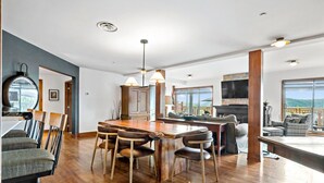 A spacious living area with a wooden dining table, chairs, and a large window offering a view of the outdoors. - Tremblant Prestige - Altitude 170-2 (Mont-Tremblant)