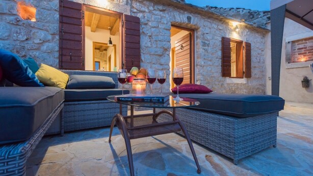 A stone building with a cozy outdoor seating area featuring wicker furniture and a table with glasses of wine. - Holiday Home Near Vrana Lake and Adriatic Sea (Benkovac)