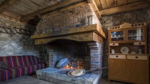 A rustic room with a brick fireplace, a wooden bench, a colorful striped sofa, and a wooden cabinet with glass doors. - Holiday Home Near Vrana Lake and Adriatic Sea (Benkovac)