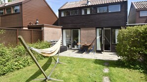 A two-story house with a brick exterior, a hammock in the yard, and a patio with outdoor furniture.