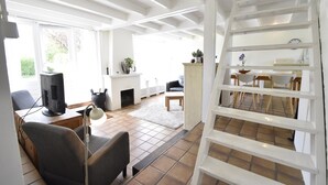 A living room with a fireplace, a dining area with a table and chairs, and a white ladder in the corner.