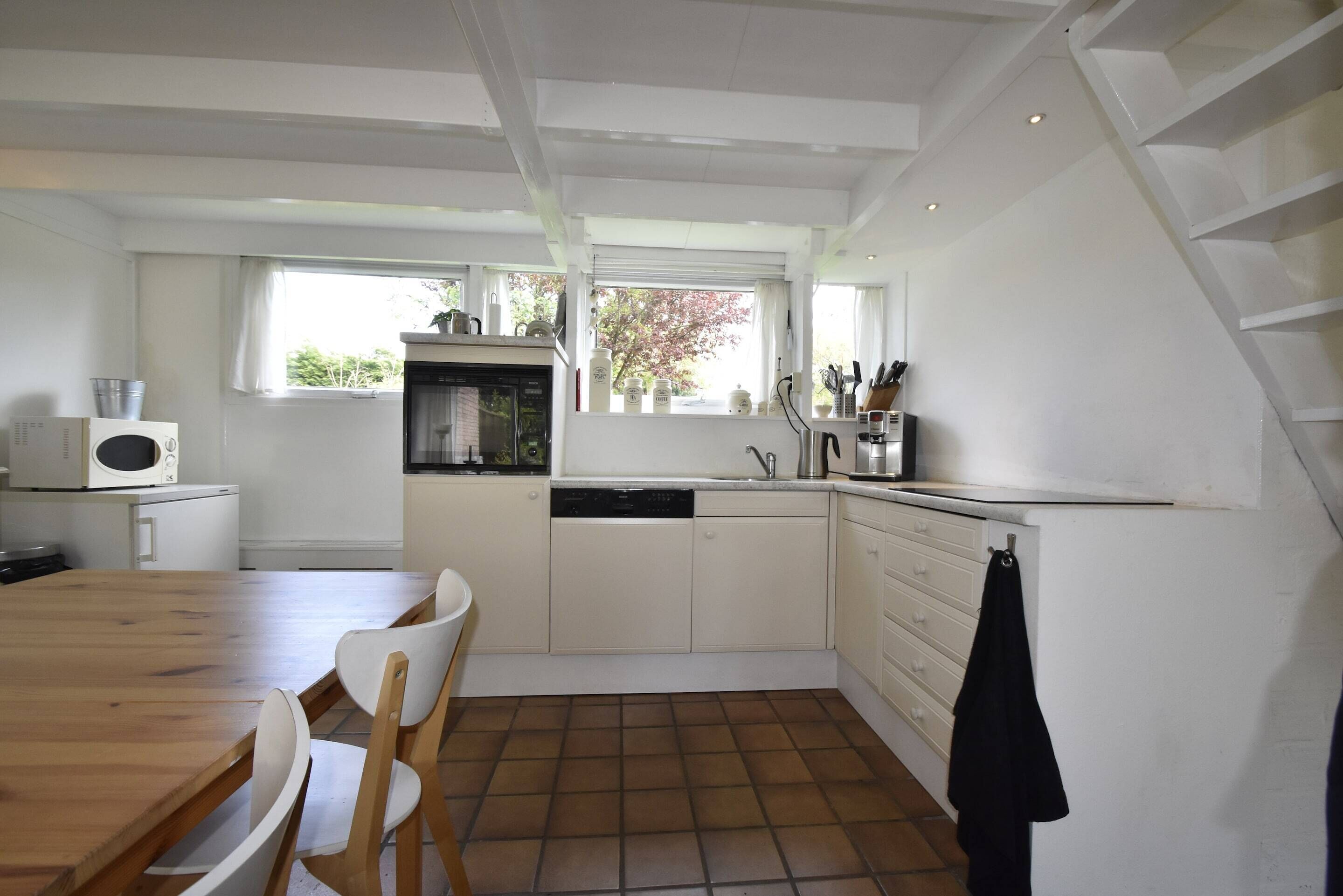 A kitchen with a dining table, chairs, a microwave, a dishwasher, and a window with a view of trees.