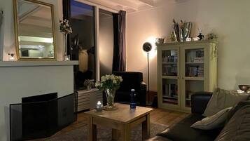 Una sala de estar con un sofá, una mesa de centro, un aparador con libros, un espejo y un ventanal corredero.
