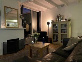 Una sala de estar con un sofá, una mesa de centro, un aparador con libros, un espejo y un ventanal corredero.