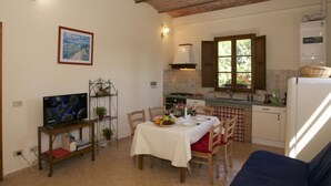 Una cocina acogedora con una mesa de comedor lista para dos personas, un televisor sobre un mueble bajo y un refrigerador.