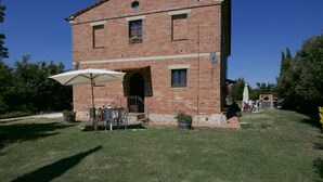 Un edificio de ladrillo con un pequeño patio que cuenta con una mesa, sillas, un paraguas blanco y plantas en macetas.