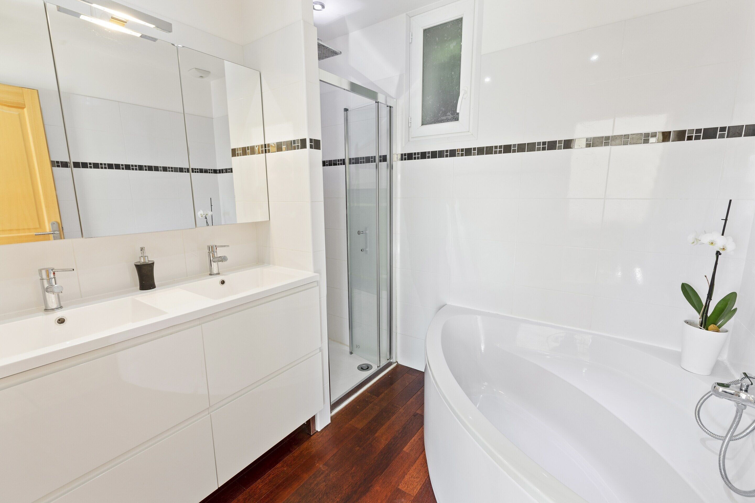 Ein modernes Badezimmer mit großem Spiegel, bodenebener Dusche, Badewanne und einer Topfpflanze.