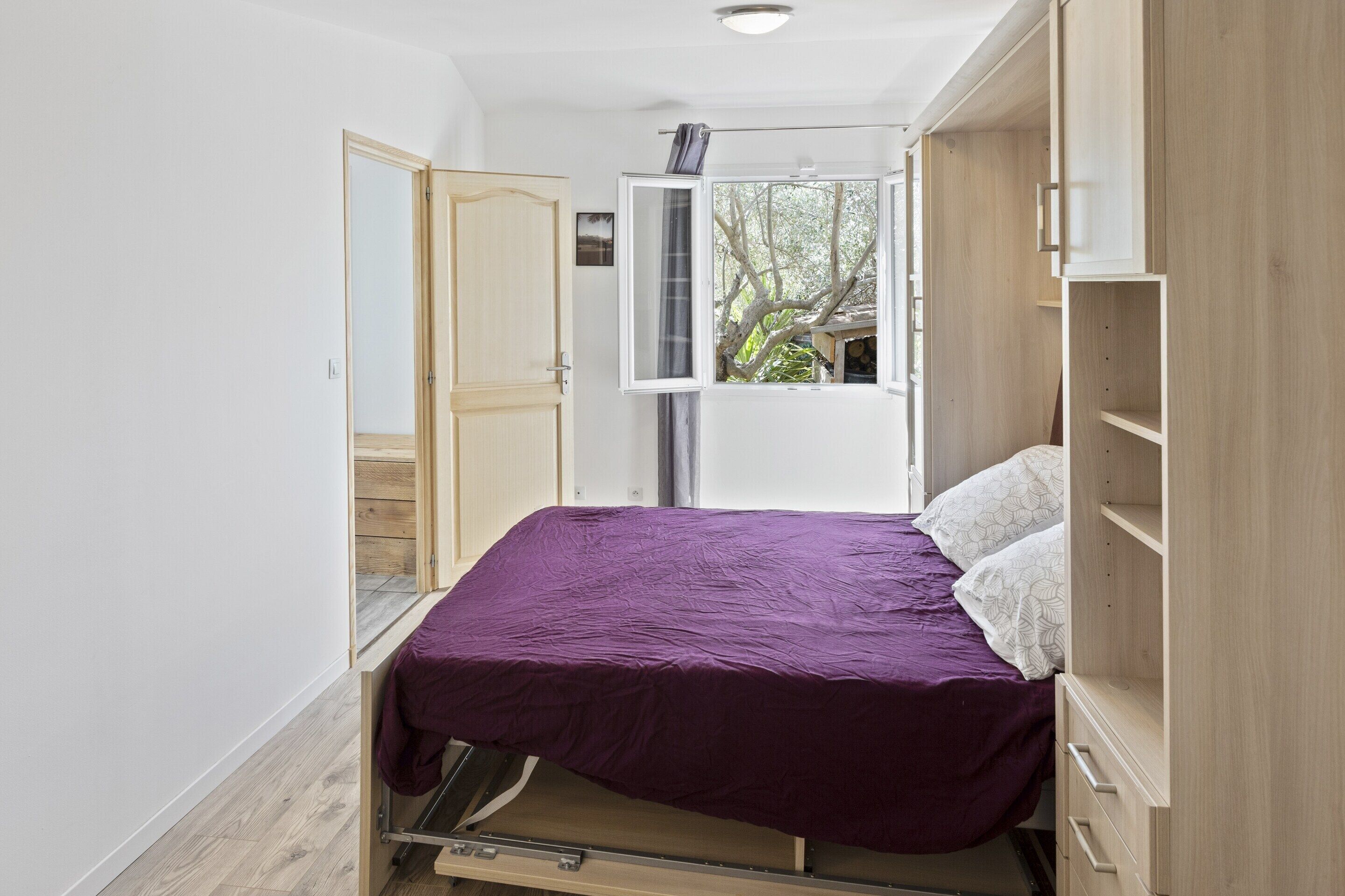Habitación compacta con cama, armario y ventana con vistas a árboles.