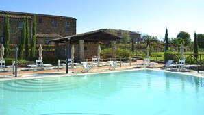 A swimming pool with lounge chairs and umbrellas, surrounded by stone buildings and greenery. - House in Tuscany Near Baratti Beach (Campiglia Marittima)