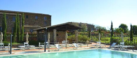 A swimming pool with lounge chairs and umbrellas, surrounded by stone buildings and greenery.