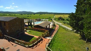 A stone building with a pool and outdoor seating area, surrounded by a well-maintained lawn and a view of rolling hills. - House in Tuscany Near Baratti Beach (Campiglia Marittima)
