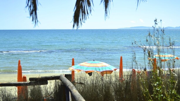 A beach with umbrellas and a wooden fence. - House in Tuscany Near Baratti Beach (Campiglia Marittima)