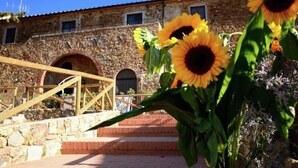 A stone building with arched doorways and a wooden staircase leading up to a brick platform. - House in Tuscany Near Baratti Beach (Campiglia Marittima)