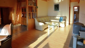 Een ruime woonkamer met een houten plafond, een bank, een salontafel en een televisie.