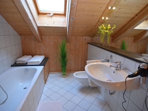 Ein Badezimmer mit Badewanne, Waschbecken und Toilette. Über der Badewanne ist ein Oberlicht, über dem Waschbecken ein Spiegel.