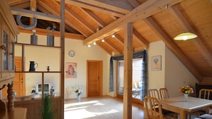 Een ruime keuken met houten balken, een zithoek met een tafel en stoelen, en uitzicht op buiten door een raam.