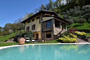 A two-story house with a stone facade, a swimming pool, and a garden with various plants and a large pot. - Flat in Villa, With Garden, Barbecue (Pisogne)