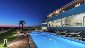 Un área de piscina moderna con sillas de descanso y una piscina iluminada al anochecer.