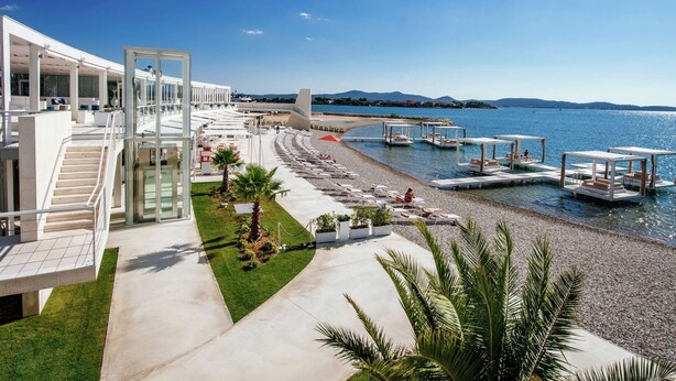 Un hotel moderno con zona de piscina, asientos exteriores y vistas al mar.