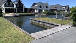 Um canal com um cais para barcos, casas com telhados inclinados e uma área gramada.