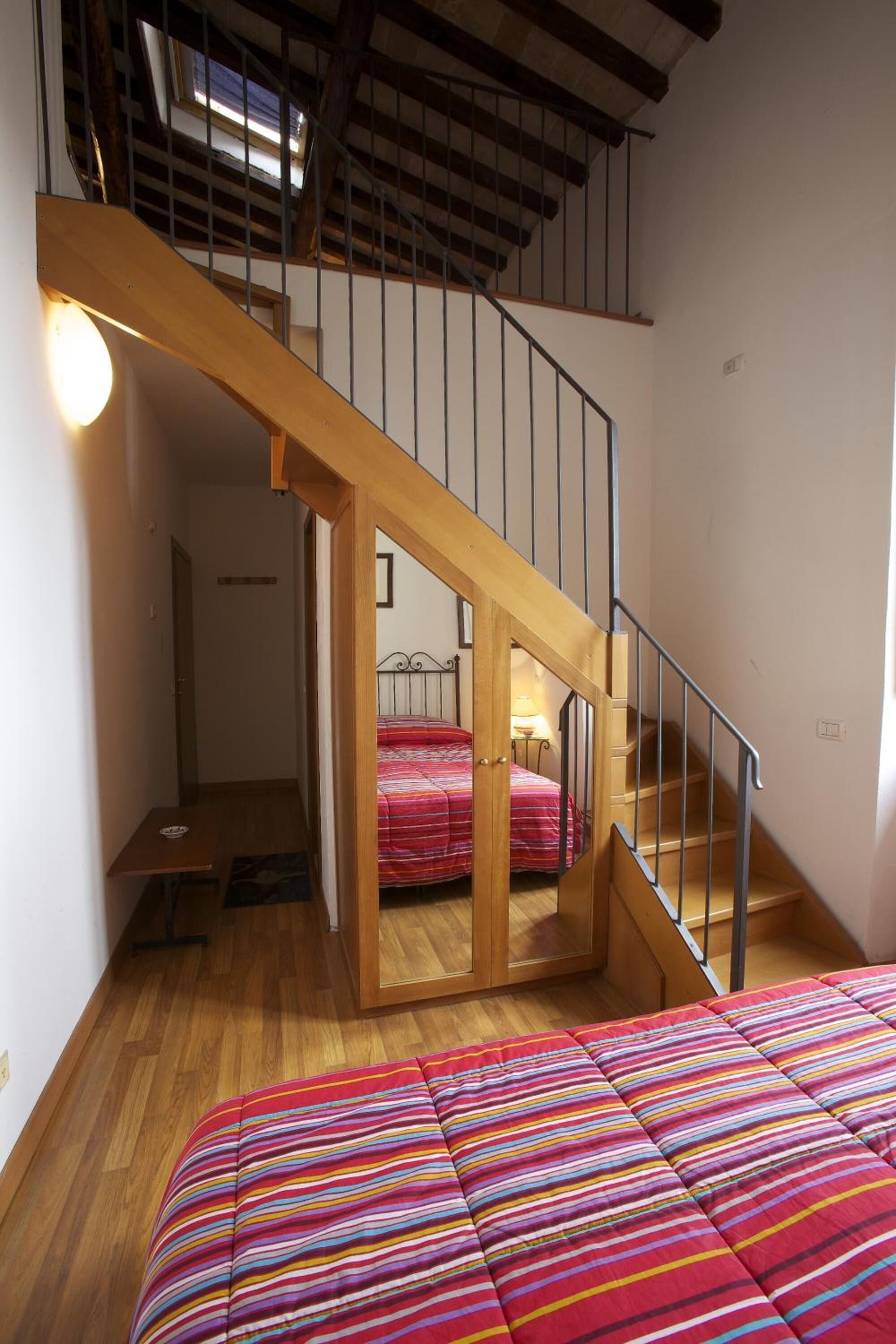 Un dormitorio con una escalera de madera, una cama con un edredón de rayas coloridas y una mesita de noche con una lámpara.