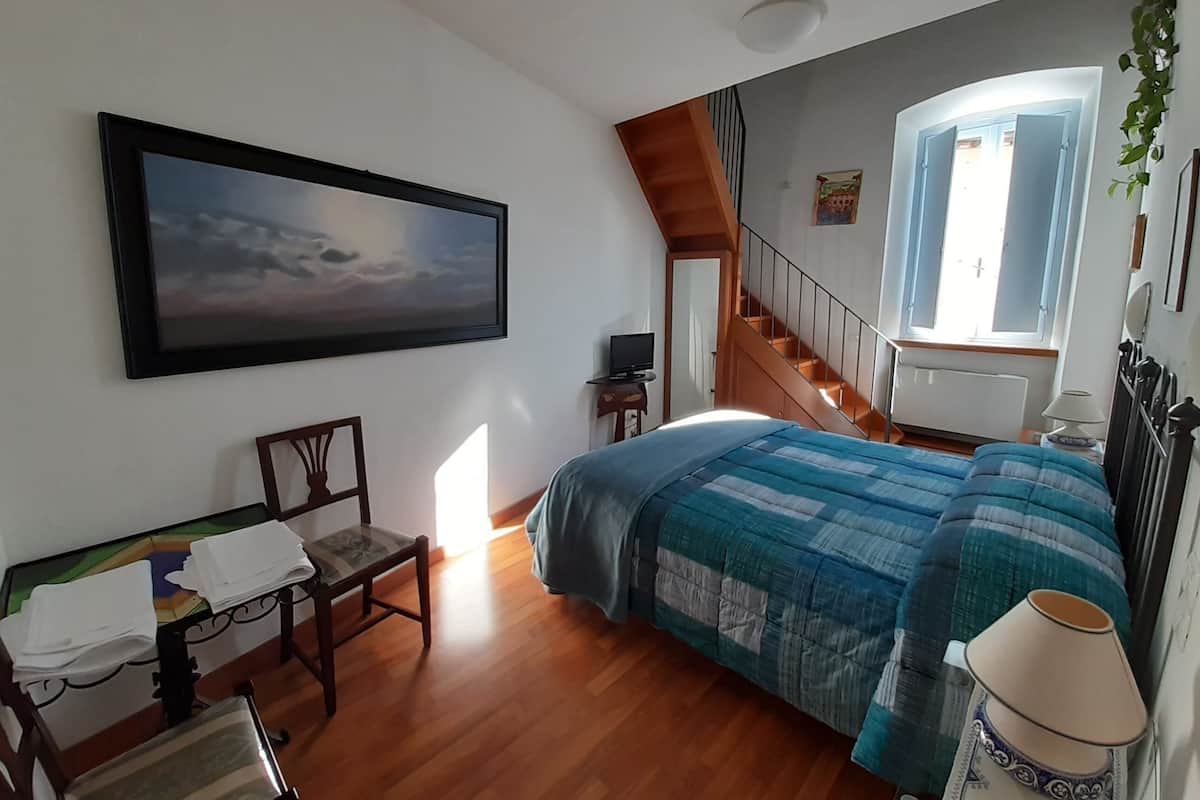 Une chambre à coucher avec un lit, un bureau, une chaise, un tableau, une fenêtre et un escalier.