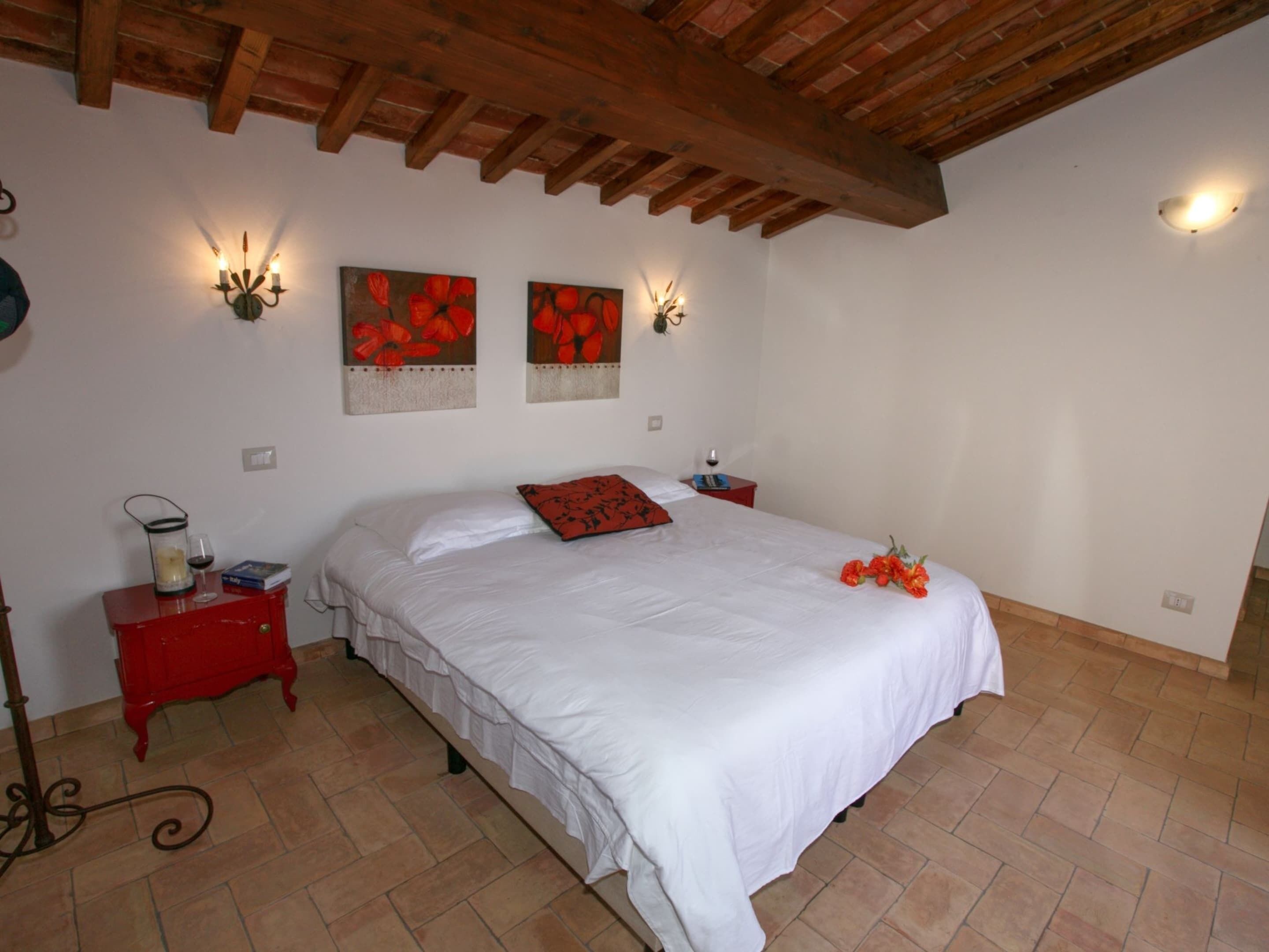 A bedroom with a large bed, a red nightstand, two wall-mounted light fixtures, and a wooden ceiling.