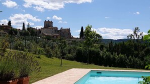 A swimming pool with a tiled deck, surrounded by greenery and a view of a historic building in the background.