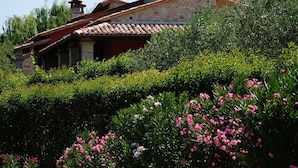 A stone building with a tiled roof, surrounded by lush greenery and flowering plants.