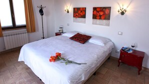 A bedroom with a large bed, two wall-mounted lamps, a radiator, and a window with curtains.