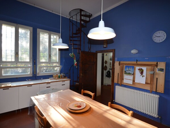 A room with a wooden table, a window with a view, a white radiator, and a wall clock. - Belvilla by OYO Villa La Commenda Nove (Faenza)