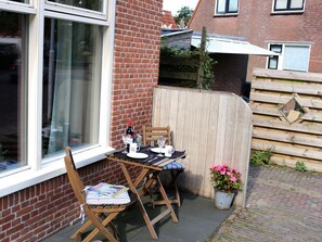 A small outdoor dining area with a table and chairs, a potted plant, and a brick wall. - Home With Vinyls, Bikes and Waterways (Easterlittens)