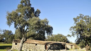 Un edificio rústico de piedra con techo de tejas, rodeado de árboles y césped.