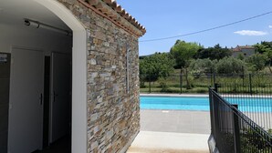 Un edificio de piedra con techo de tejas, piscina y zona vallada.