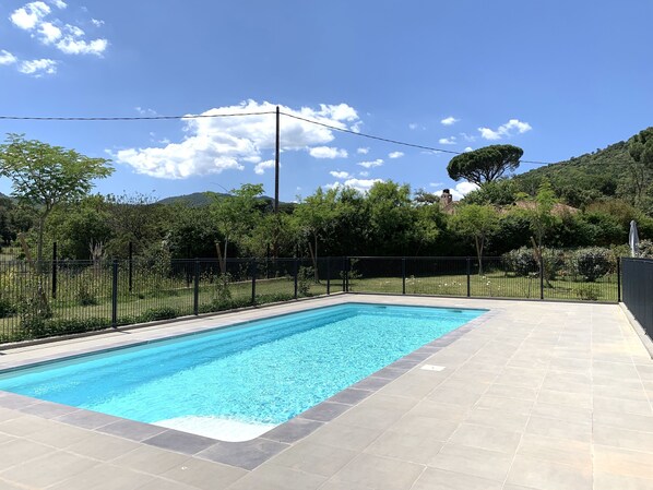 A rectangular swimming pool with a tiled deck, surrounded by a black metal fence and lush greenery. - L'Oustalet charming apartment in the heart of the village (Le Plan-de-la-Tour)