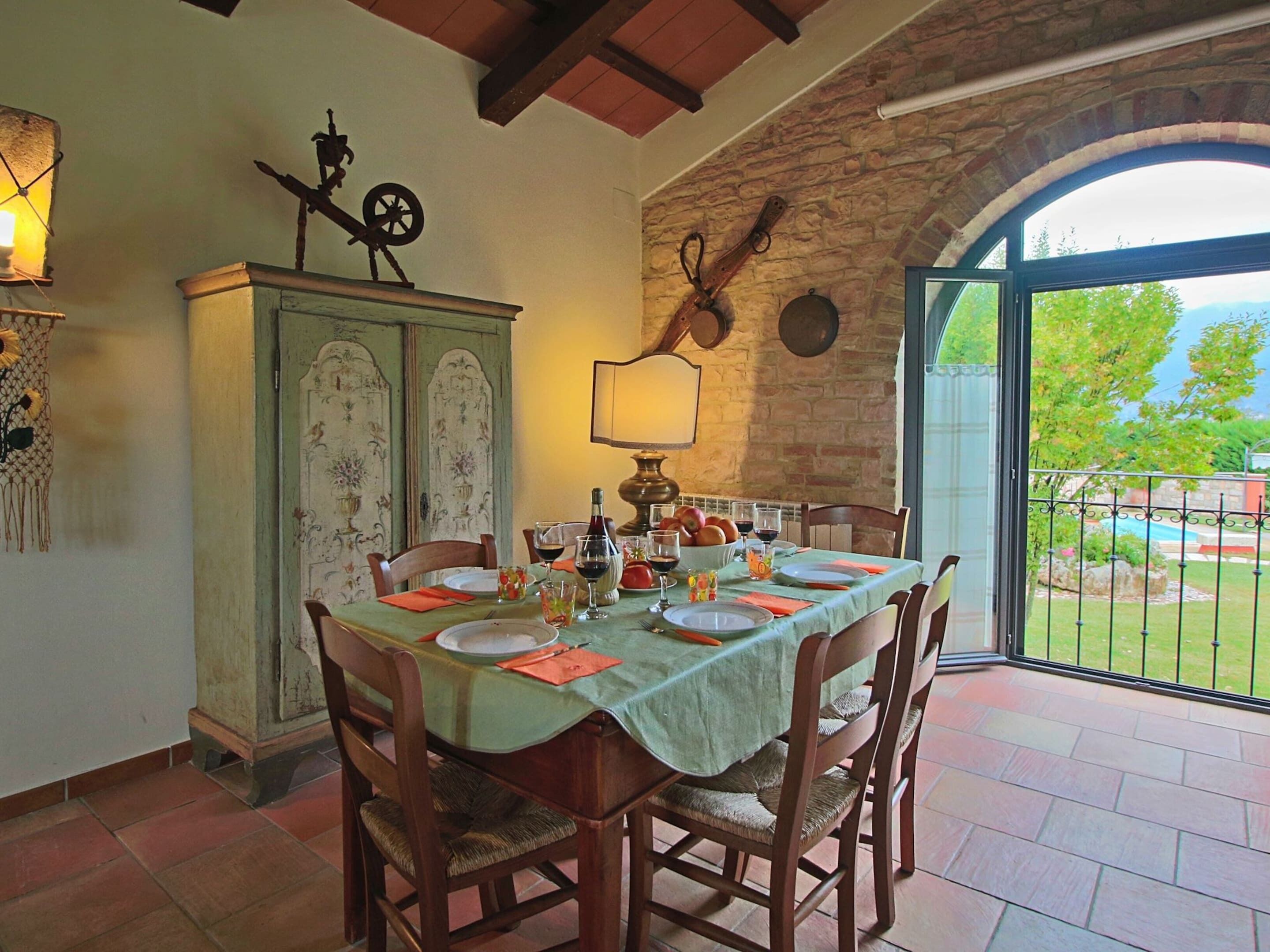 A dining area with a table set for four, a wooden cabinet with decorative panels, and a view of the outdoors through a glass door.
