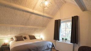 A bedroom with a large bed, a window with curtains, a chair, and a radiator. - Spacious Villa Near Arcen in a Wooded Area (Arcen)