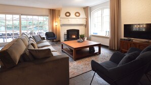 A living room with a fireplace, a sofa, a coffee table, and a TV. - Spacious Villa Near Arcen in a Wooded Area (Arcen)