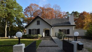 A two-story house with a brick pathway leading to the entrance, surrounded by trees and a fence. - Spacious Villa Near Arcen in a Wooded Area (Arcen)